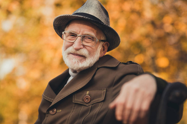 Closeup photo of funny glad old pensioner grey haired grandpa central park walk enjoy sunny day warm weather sit bench break pause wear stylish autumn jacket hat specs colorful street outside - Foto, Bild