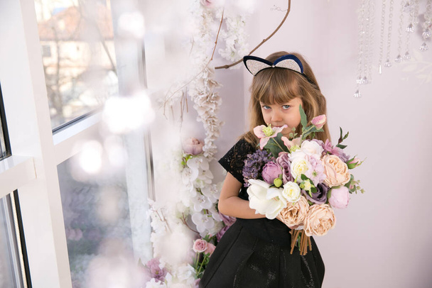 Beautiful little girl in black sleeveless top wearing cat ear headband and holding a bunch of flowers - Foto, afbeelding