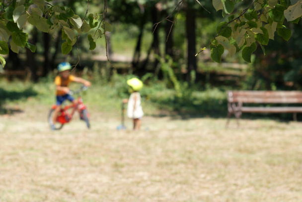 θολή φωτογραφία, μικρά παιδιά στο πάρκο με ποδήλατο και σκούτερ - Φωτογραφία, εικόνα