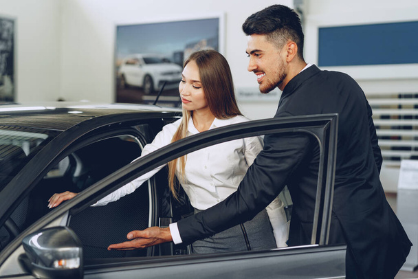 Man car dealer showing a woman buyer a new car - Fotoğraf, Görsel