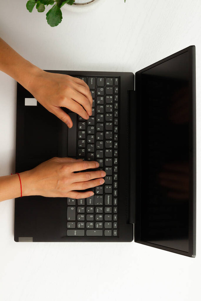 female hands are typing text on laptop keyboard on white wooden table background - Photo, Image