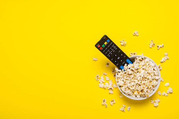 TV remote control, TV tuner lie in a bowl with popcorn on a yellow background. Concept series, film, sports. Banner. Flat lay, top view. - Photo, Image