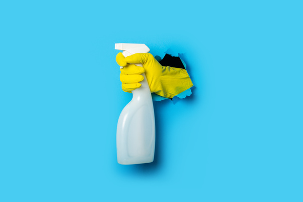 Hand in yellow gloves holding spray on a bright blue background. - Photo, Image