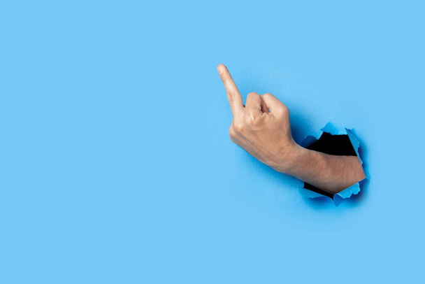 Hand shows the gesture of the middle finger on a blue background. Offensive gesture, fuck off, leave me alone. - Foto, imagen