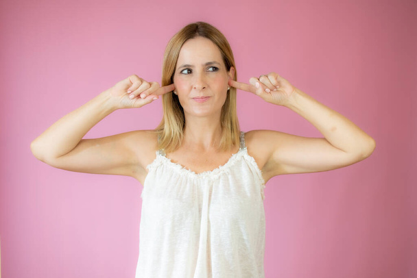 Smiling woman covering her ears on pink background - Photo, Image