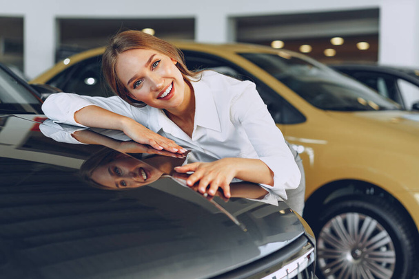 Beautiful young woman touching her new car with pleasure - Фото, изображение