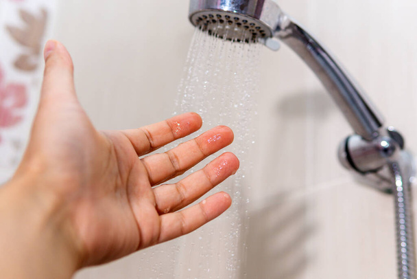 víz közeli háttér. Közelkép egy férfi kézzel ellenőrizze a víz hőmérsékletét a zuhany alatt kézi zuhanyzóval - Fotó, kép