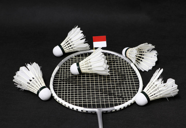 Mini Indonesia vlag plakken op de shuttlecock op het net van badminton racket en vier shuttlecocks eromheen op de zwarte vloer. - Foto, afbeelding