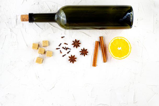 Fles wijn en kruiden op witte achtergrond. Ingrediënten voor een glühwein. Kaneel, anijssterren, sinaasappel, bruine suiker, kruidnagel. Kerst warme drank - Foto, afbeelding