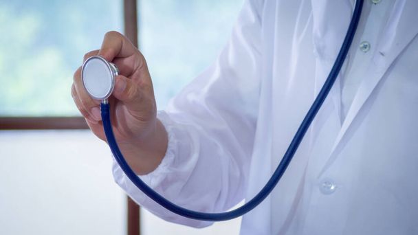 Male medicine doctor hand holding stethoscope against of chest on hospital background. Physician ready to examine patient. Medical and patient care concept. - Photo, Image