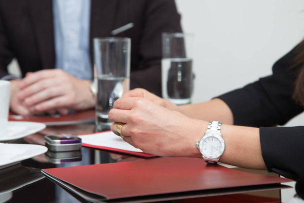 people in a meeting, approach to the table where there are documents, glasses of water and the hands of a person with a watch on the wrist - 写真・画像