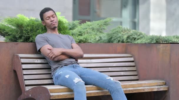 cansado joven africano hombre takin siesta en banco al aire libre - Metraje, vídeo