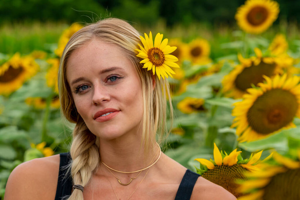 Ein hinreißendes blondes Model posiert draußen in einem Sonnenblumenfeld, während es einen Sommertag genießt - Foto, Bild