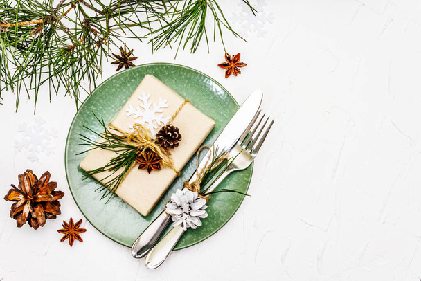 Boże Narodzenie lub Nowy Rok nakrycie stołu. Sztućce świąteczne, ceramiczne talerze ze świeżą gałązką sosny, szyszki, zero odpadów prezentów i anyż gwiazdkowy. Białe tło kit, widok z góry - Zdjęcie, obraz