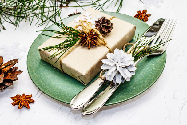Boże Narodzenie lub Nowy Rok nakrycie stołu. Sztućce świąteczne, ceramiczne talerze ze świeżą gałązką sosny, szyszki, zero odpadów prezentów i anyż gwiazdkowy. Białe tło kit, zbliżenie - Zdjęcie, obraz