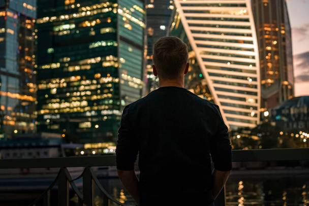 Портрет бізнесмена в чорному светрі з видом нічного освітлювального бізнесу хмарочоси в Москві, фотографія з шумом і стилем сірості - Фото, зображення