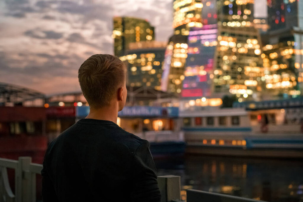 Retrato de un hombre de negocios en un suéter negro con vistas a los rascacielos de negocios de iluminación nocturna en Moscú, foto con ruido y estilo granulado - Foto, Imagen