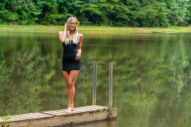 Een prachtig blond model poseert buiten in de buurt van een vijver terwijl u geniet van een zomerse dag - Foto, afbeelding