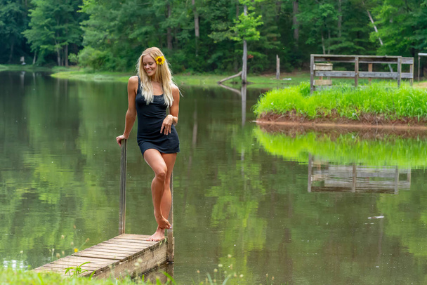 Розкішна блондинка модель позує на відкритому повітрі біля ставка, насолоджуючись літнім днем
 - Фото, зображення