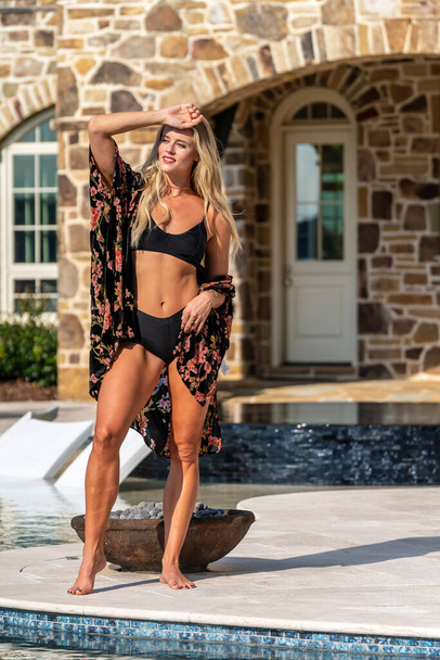 Egy gyönyörű szőke bikini modell élvezi a nyári napokat a medencénél. - Fotó, kép
