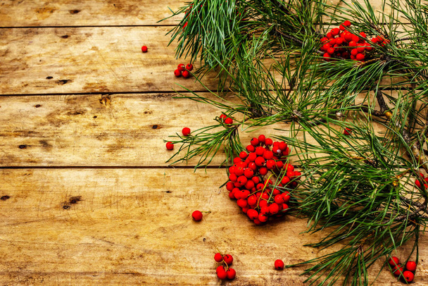 Christmas or New Year concept. Fresh pine branches, ripe rowan berries, snowflakes and pine cones. Old wooden background, copy space - Photo, image