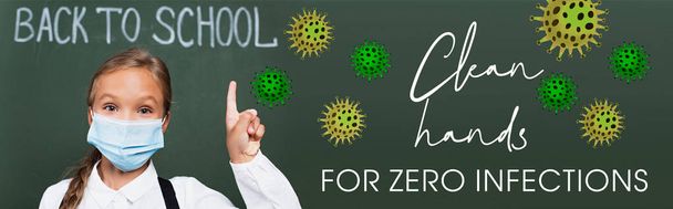 horizontal image of schoolgirl in medical mask pointing with finger near chalkboard and clean hands for zero infections lettering in classroom  - Photo, Image