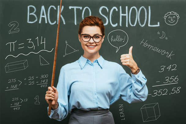 geometry teacher with pointing stick showing thumb up near chalkboard with back to school lettering and illustration  - Zdjęcie, obraz