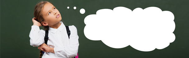 πανοραμική λήψη στοχαστική μαθήτρια αγγίζοντας το κεφάλι και κοιτάζοντας προς τα πάνω κοντά στο chalkboard με την εικόνα φυσαλίδων σκέψης  - Φωτογραφία, εικόνα