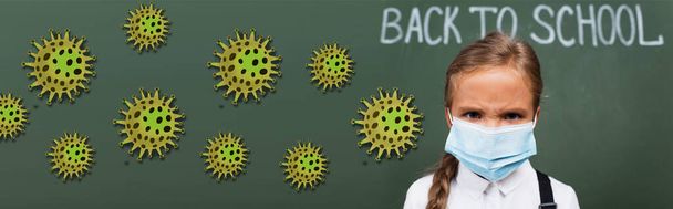 horizontal image of displeased schoolgirl in medical mask near back to school lettering  and virus illustration on chalkboard - Photo, Image