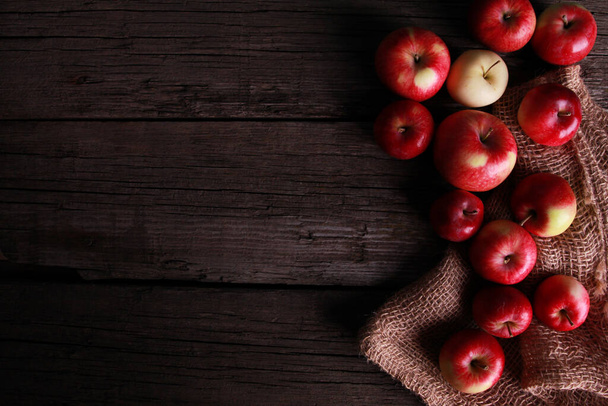 Red ripe apples, burlap sackcloth on rough rustic old wooden board. Top view, copy space. Natural organic food, agriculture, horticulture, harvest season concept - Photo, Image