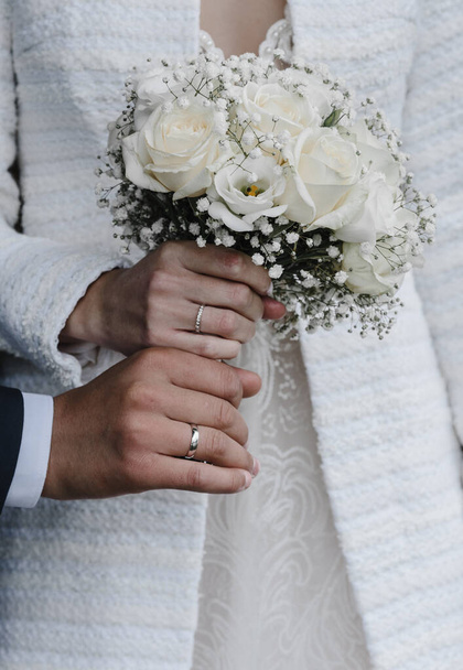 mano de novias con un elegante anillo de bodas con diamantes de oro blanco en un ramo de sus peonías - Foto, Imagen