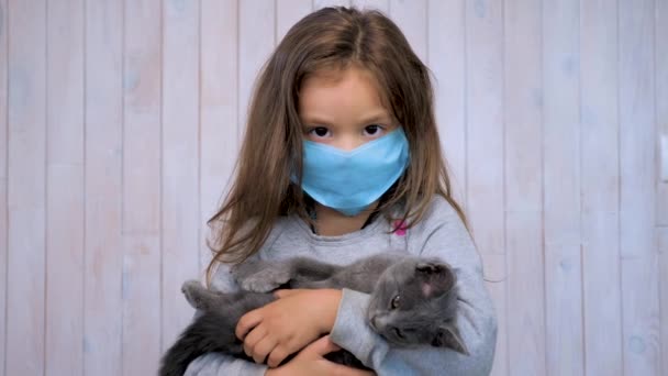 Leven tijdens een coronavirus pandemie. School tijdens quarantaine. Regio 's van de Rode Zone. Meisje met een katje met een medisch wegwerpmasker. Hij droeg een gezichtsmasker. Infectiepreventie en bestrijding van IPC - Video