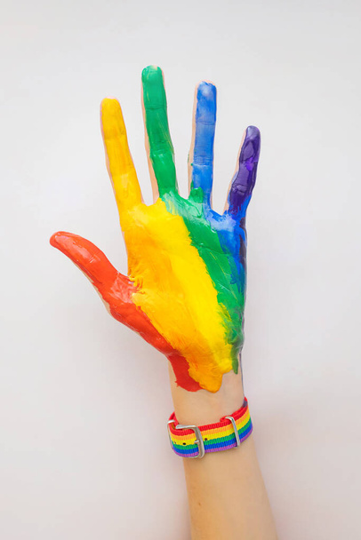 A woman's hand is smeared with paint and a bracelet in the colors of the LGBT rainbow. The concept of love, sexual tolerance, LGBT pride, same-sex relationships, homosexuality. - Foto, Imagen