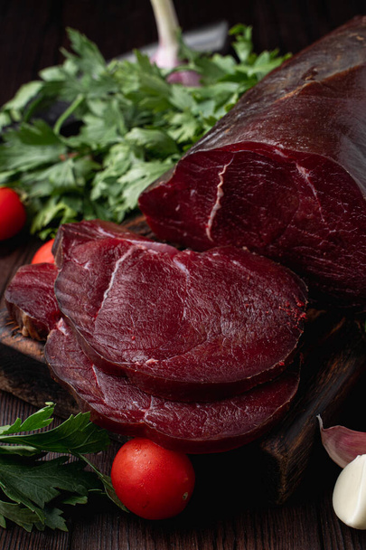Raw tenderloin, sliced and surrounded with herbs, on dark background, photography for a market catalogue - Fotó, kép