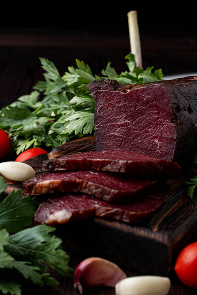 Smoked and dried mignon, juicy and yummy, on dark background with herbs and spices around, ad photo - Fotó, kép