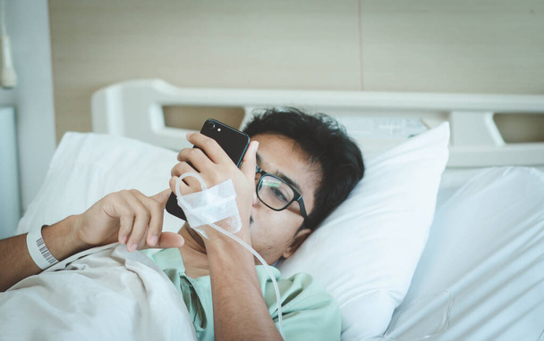 Un paciente masculino usa un teléfono inteligente para las redes sociales y contacta a un familiar mientras está en el hospital. Recuperarse de covid-19 pandémico o virus de la corona. Enfoque selectivo. - Foto, imagen