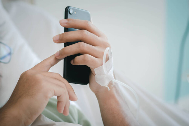 Mężczyzna korzysta ze smartfona w mediach społecznościowych i kontaktuje się z rodziną w szpitalu. Wyzdrowienie po pandemii wirusa covid-19 lub korony. - Zdjęcie, obraz