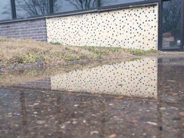 Een witte tegelwand weerspiegelt in een plas op een regenachtige dag - Foto, afbeelding