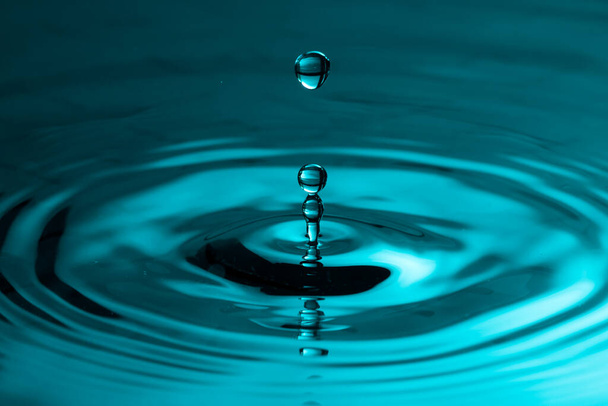 Perfect water drop splashing into smooth water causing ripples in a calm surface - Photo, Image