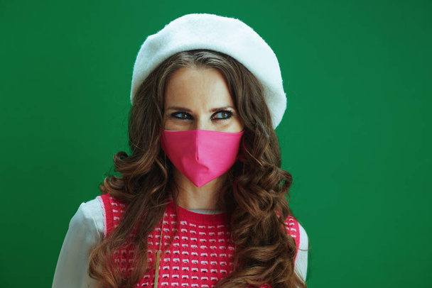 Life during coronavirus pandemic. pensive modern woman in pink sleeveless shirt with pink medical mask against green background. - Φωτογραφία, εικόνα