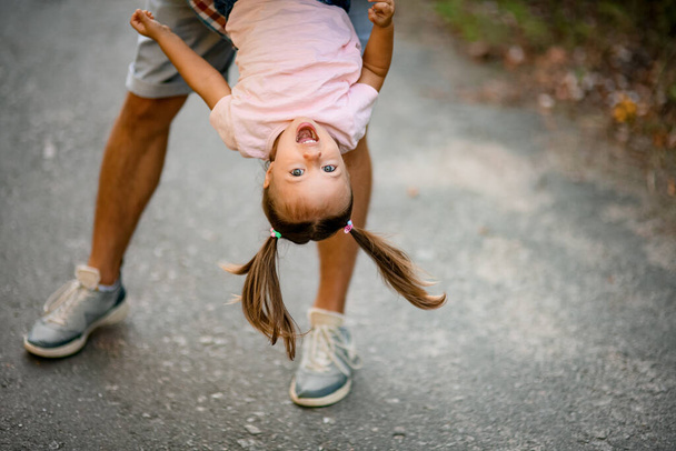 view on face of happy girl in pink t-shirt which her father hold upside down and swing her - 写真・画像