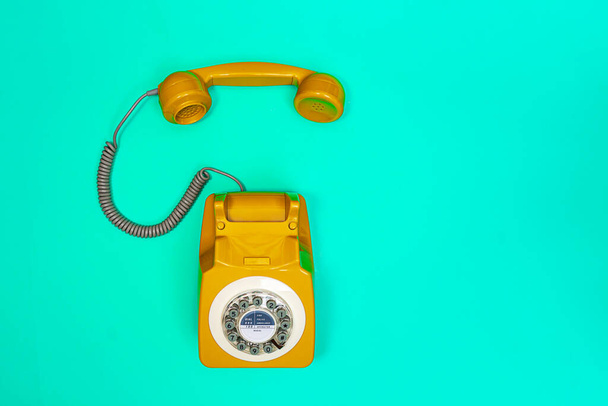Yellow handset of a telephone on a green mint background.  - Fotó, kép