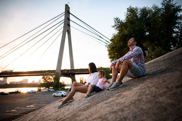 happy couple with small cute child rest near the river - 写真・画像