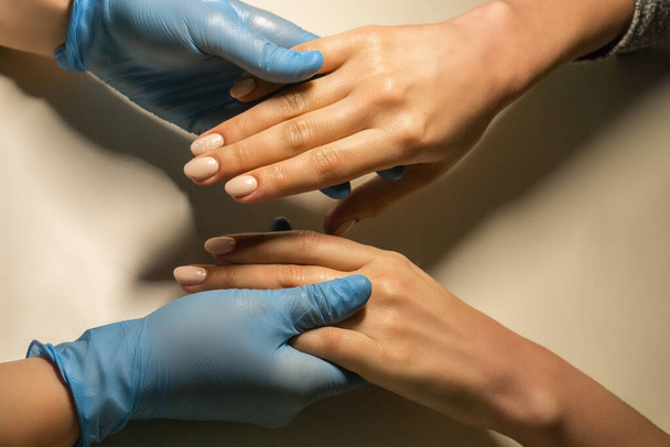 Manicure in handschoenen houdt handen van de klanten hand. Schoonheidsbehandeling concept. Salon manicure cursussen.  - Foto, afbeelding