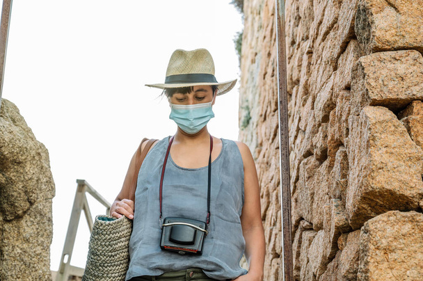 Mulher descendo as escadas em férias relaxante, com chapéu, câmera e máscara - Foto, Imagem