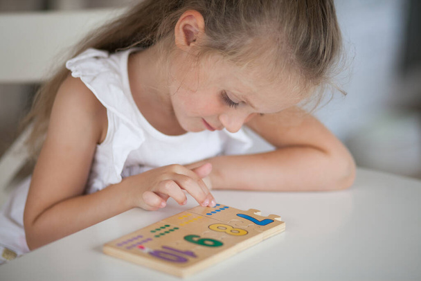 テーブルに座っている間、幼稚園の学校の準備をしている木製の数学的な多色の数字で教育ゲームをプレイする小さなかわいい未就学児の女の子。学校のコンセプトに戻る - 写真・画像