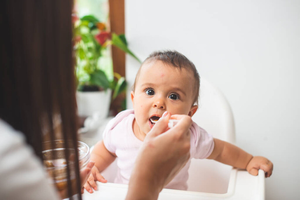 Mother feed her little daughter with a spoon - Fotoğraf, Görsel