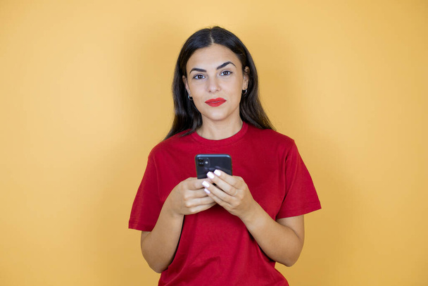 Young beautiful woman over isolated yellow background chatting with her phone. - Foto, Imagen