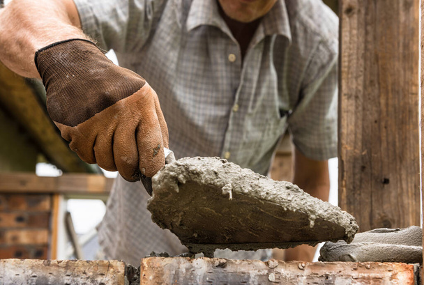 Een arbeider brengt een mortel met een troffel aan op de baksteen.. - Foto, afbeelding