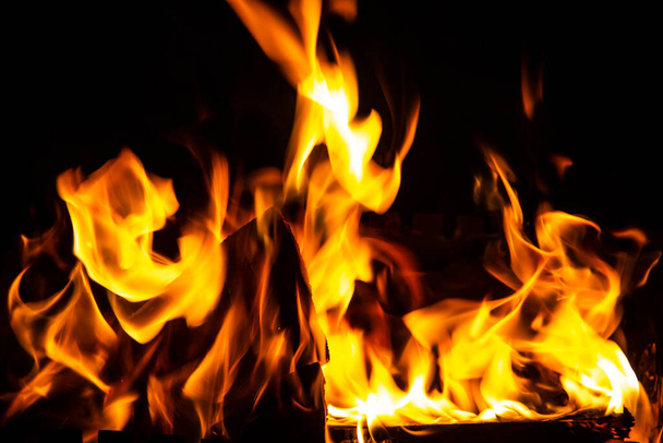 Vuur op een donkere achtergrond. Vuur van brandhout van dichtbij. Vlammende brandende vonken van dichtbij, vuurpatronen. Rood en oranje helse gloed van vuur in het donker. - Foto, afbeelding